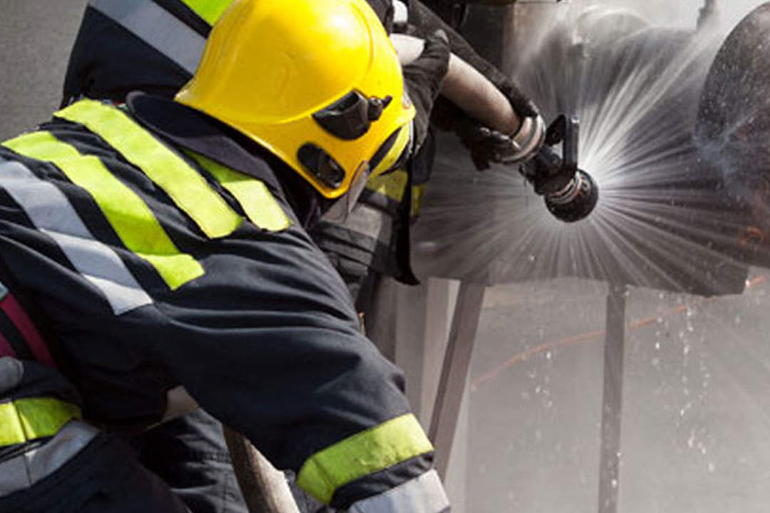 Portrait of a firefighter in safety helmet and oxygen mask holding a chainsaw