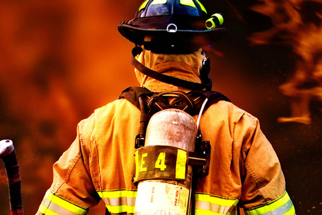 Fireman wearing protective uniform standing next to a fire engine in a garage of a fire department